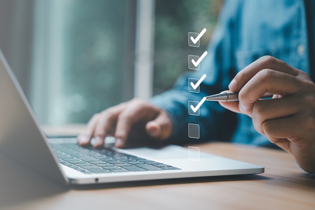 Man ticking off boxes on rendered list next to laptop to represent automating admin tasks