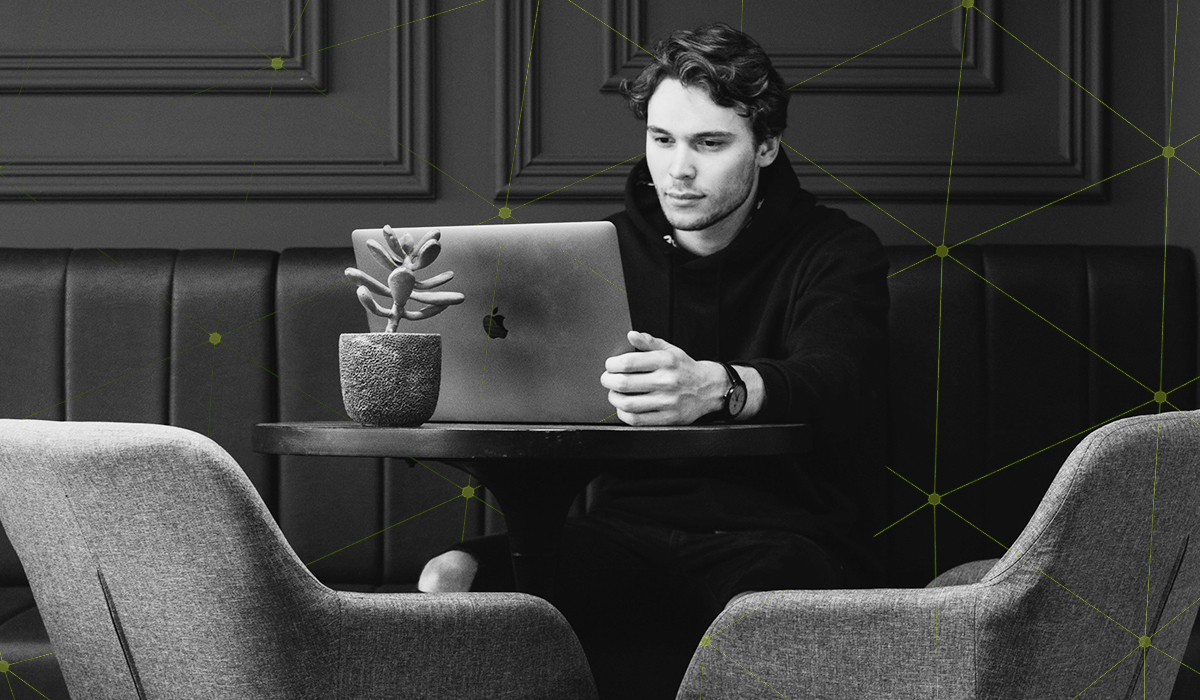 Black and white photo of a man sitting at a booth working on mac laptop