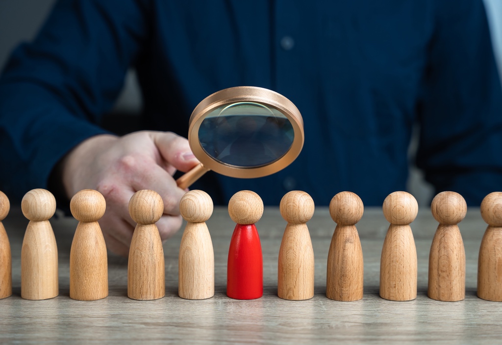 Man holding magnifying glass over one red figuring in line of many to represent users finding AI Overviews ahead of traditional search results